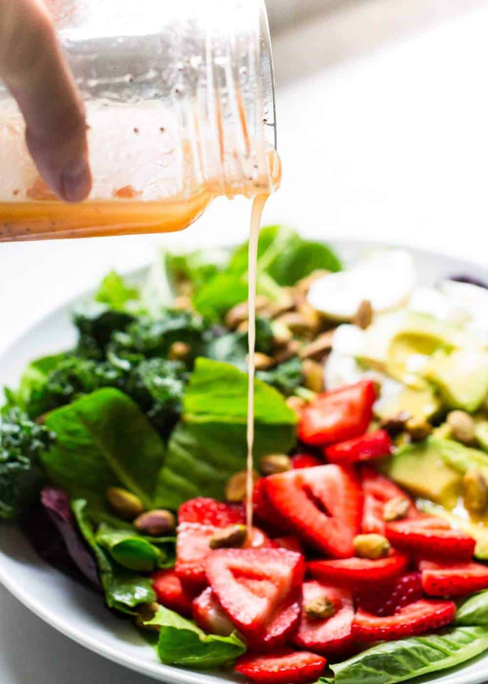 Pouring poppyseed dressing over strawberry burrata salad.