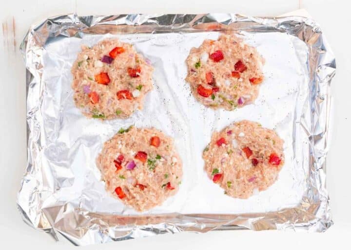 4 greek chicken burger patties on a foil lined baking sheet 