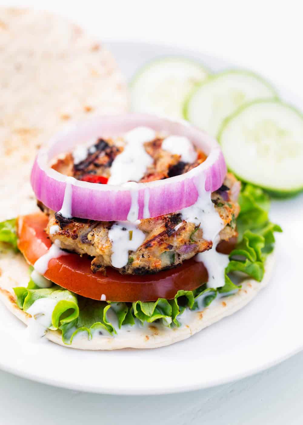 Greek chicken burger on a flatbread with lettuce, tomato and onion.