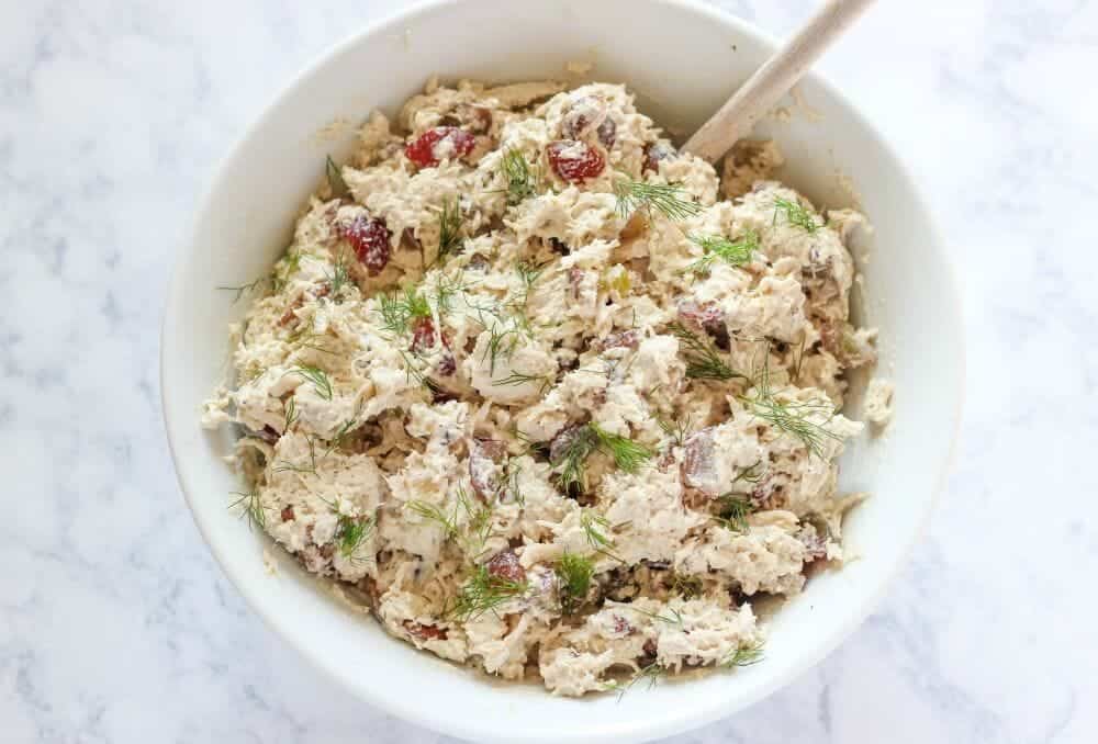 Shredded chicken salad in a white bowl with fresh dill on top.