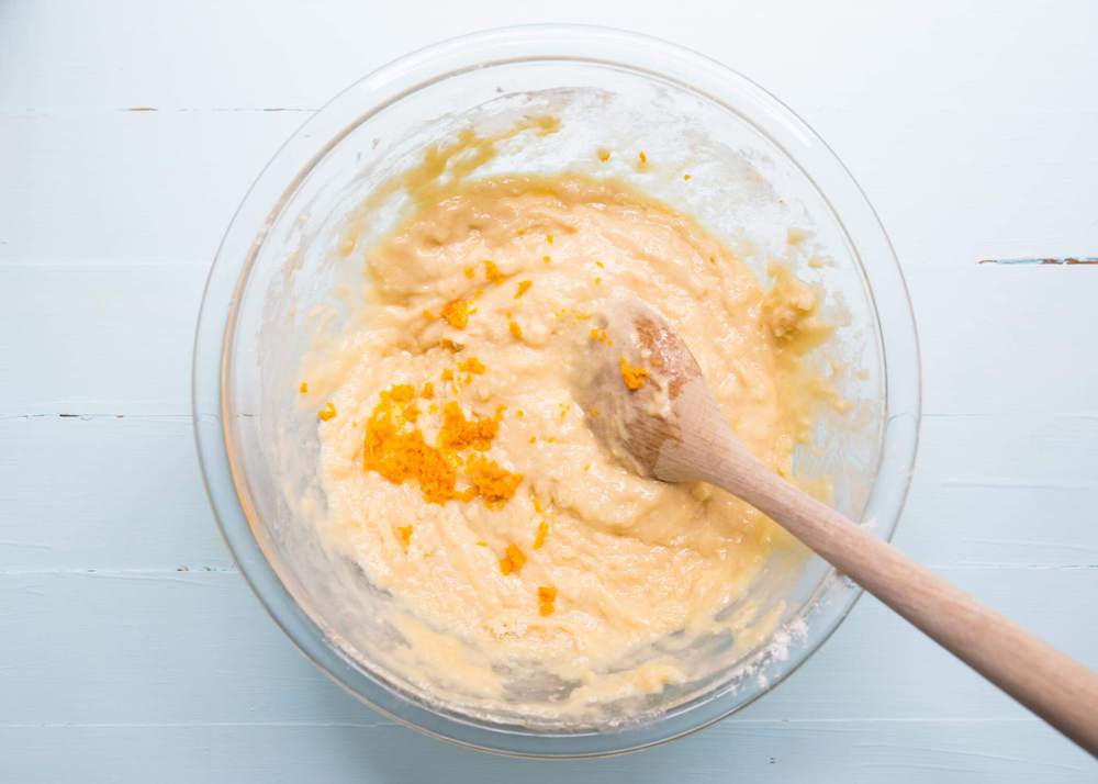 Mixing together orange muffin ingredients in a bowl with a wooden spoon.