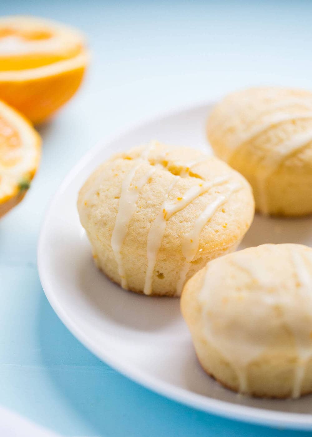 Glazed orange muffins on a white plate.