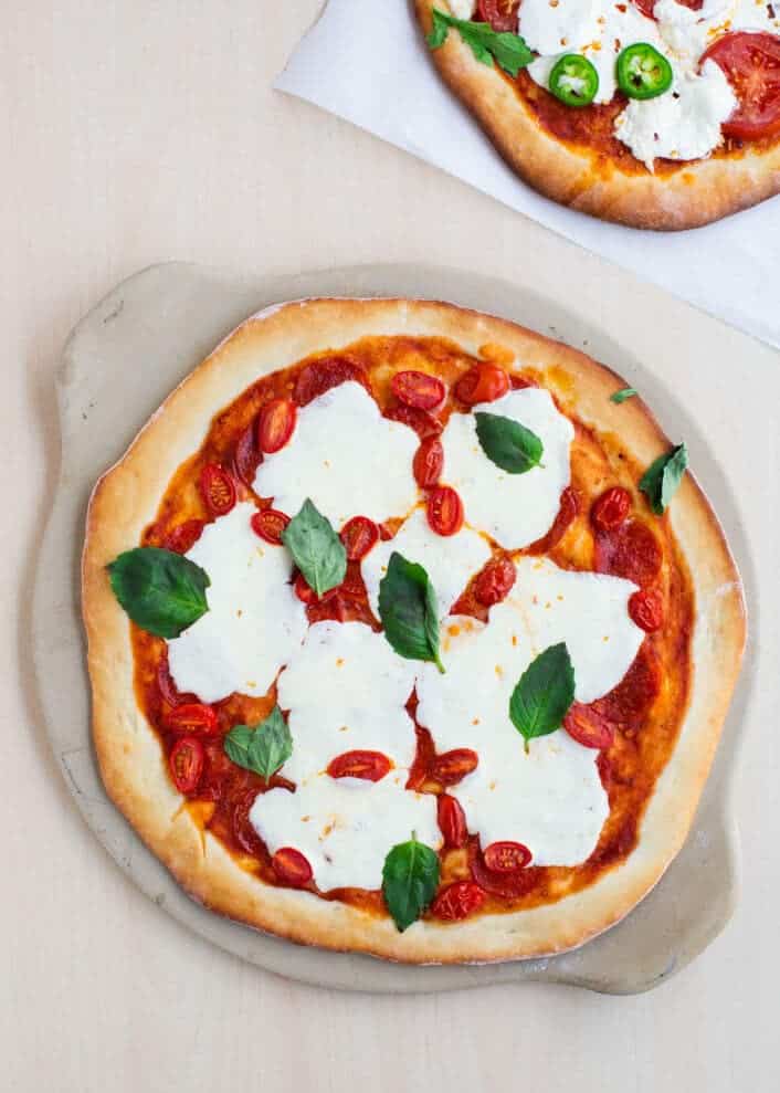 Baked homemade pizza dough with sauce, cheese, basil and tomatoes.