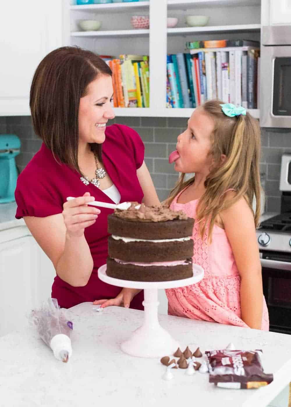 woman spreading chocolate frosting onto Neapolitan cake with daughter 