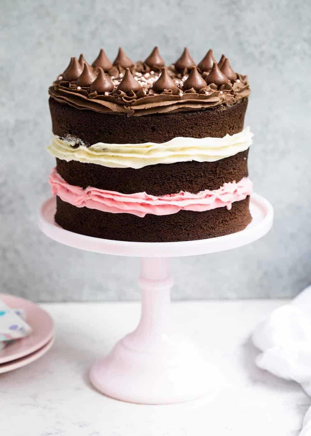 Neapolitan cake with layers of chocolate, vanilla and strawberry buttercream frosting. A classic ice cream flavor turned into a delicious and beautiful cake! Neapolitan cake on a white cake stand