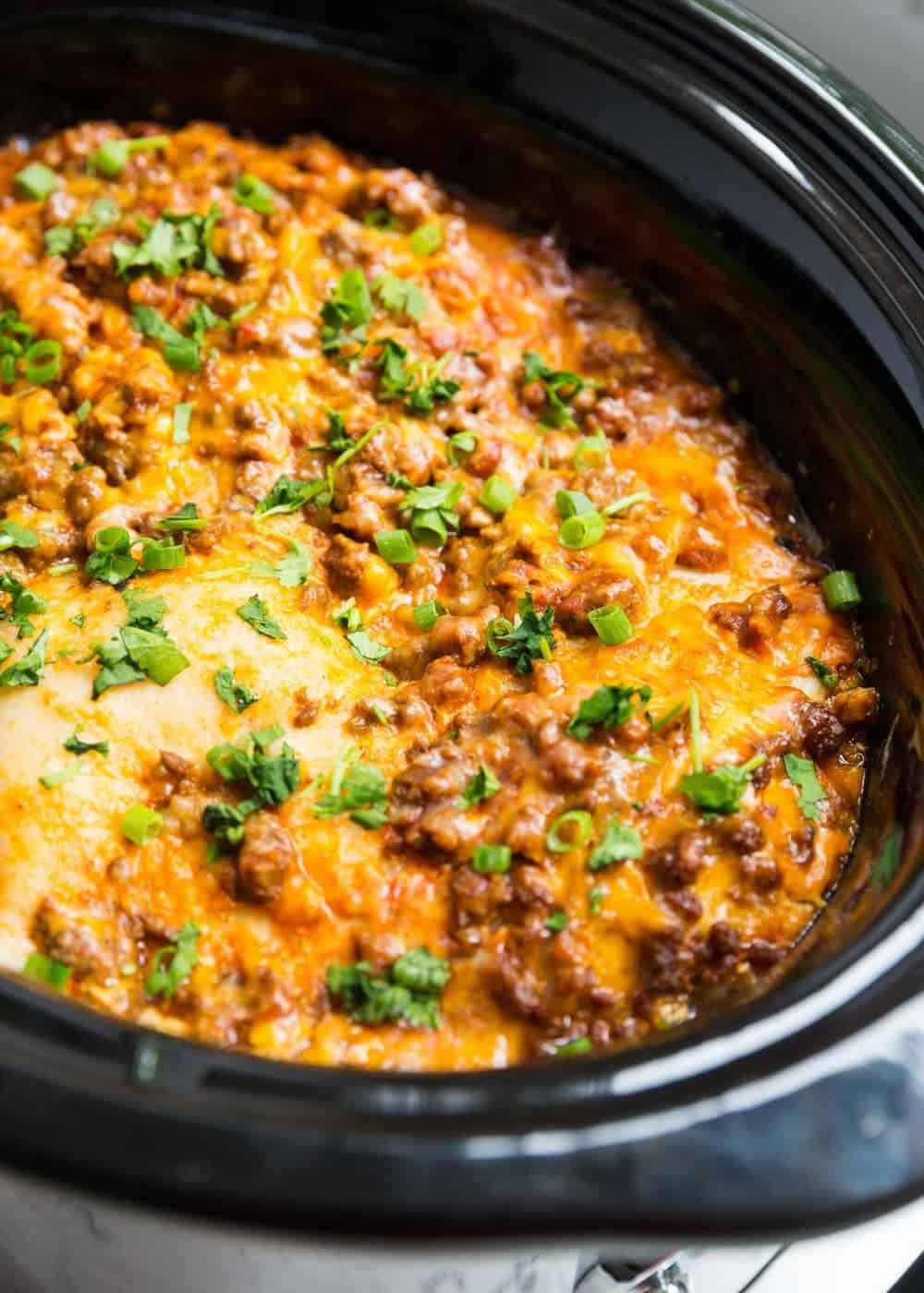 Taco lasagna in crockpot topped with sliced green onions and cilantro.