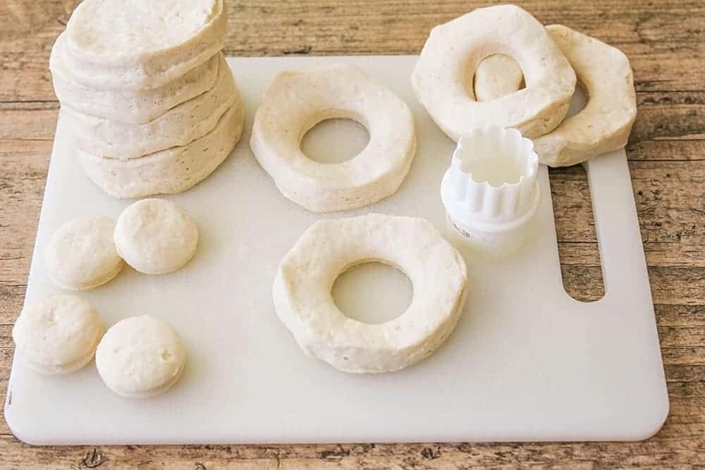 cutting centers out of biscuit dough pieces for maple donuts 
