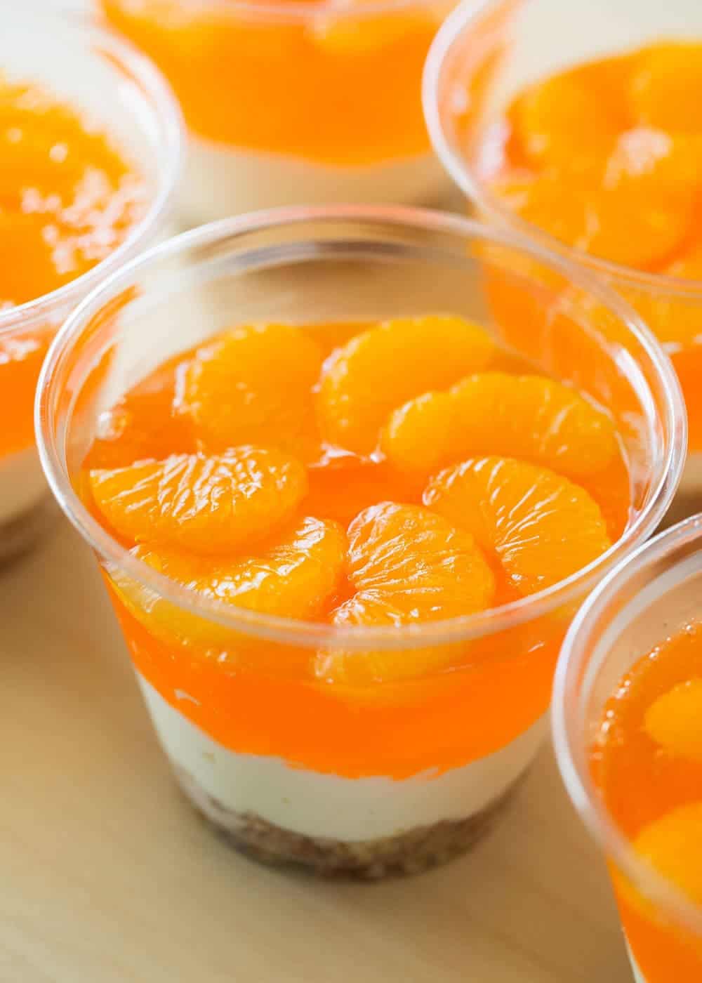 Orange pretzel salad in a clear cup with mandarins on top.