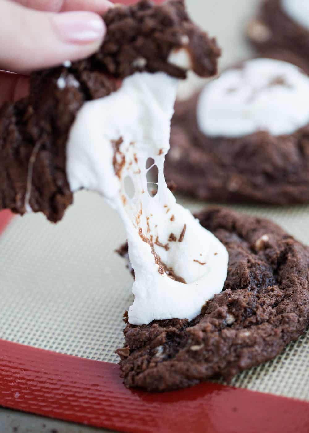 breaking apart a hot chocolate cookie with gooey marshmallow in middle 