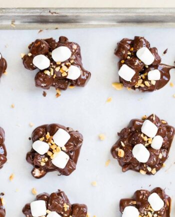 Rocky road candy clusters with chocolate, marshmallow and peanuts on a parchment lined baking sheet.