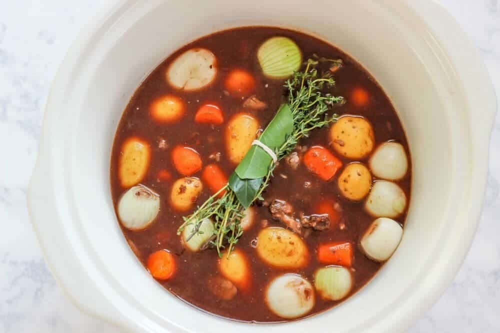 adding the vegetables and cooking liquid to crockpot for beef bourguignon