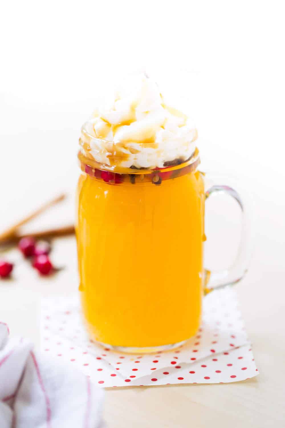 Wassail in glass mug with whipped cream and caramel sauce.