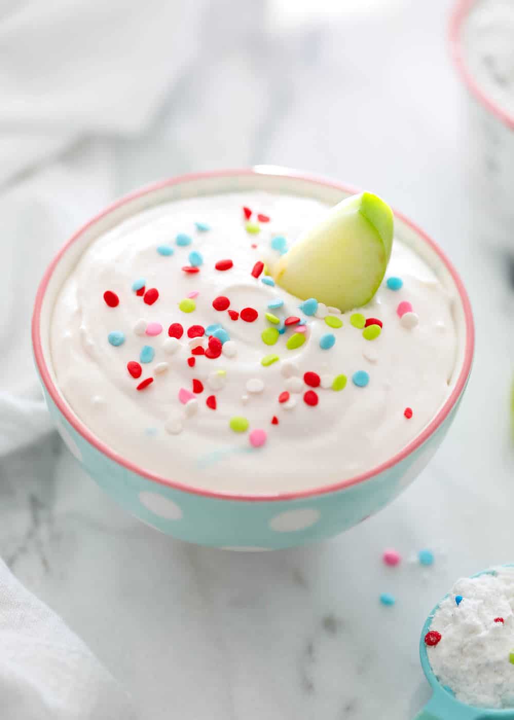 bowl of funfetti dip with sprinkles and a green apple slice 
