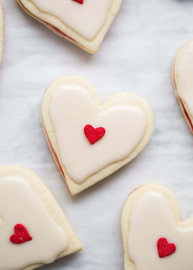 Heart Shaped Empire Cookies sandwiched with a raspberry jam filling and topped with an almond glaze. The perfect Valentine's Day dessert.