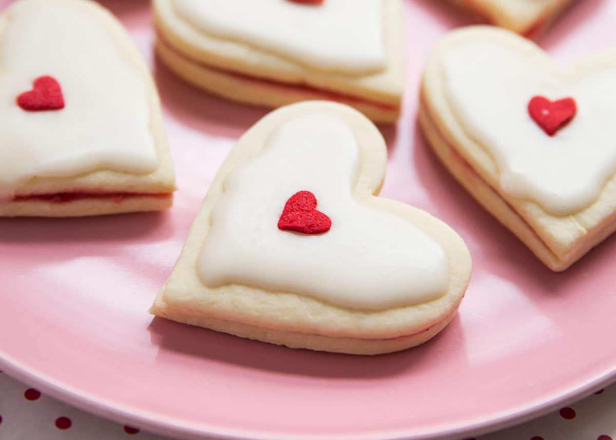 Heart shaped empire biscuits (AKA imperial cookies) sandwiched with a raspberry jam filling and topped with a powdered sugar almond icing. The perfect Valentine's Day dessert! Heart shaped empire biscuit.