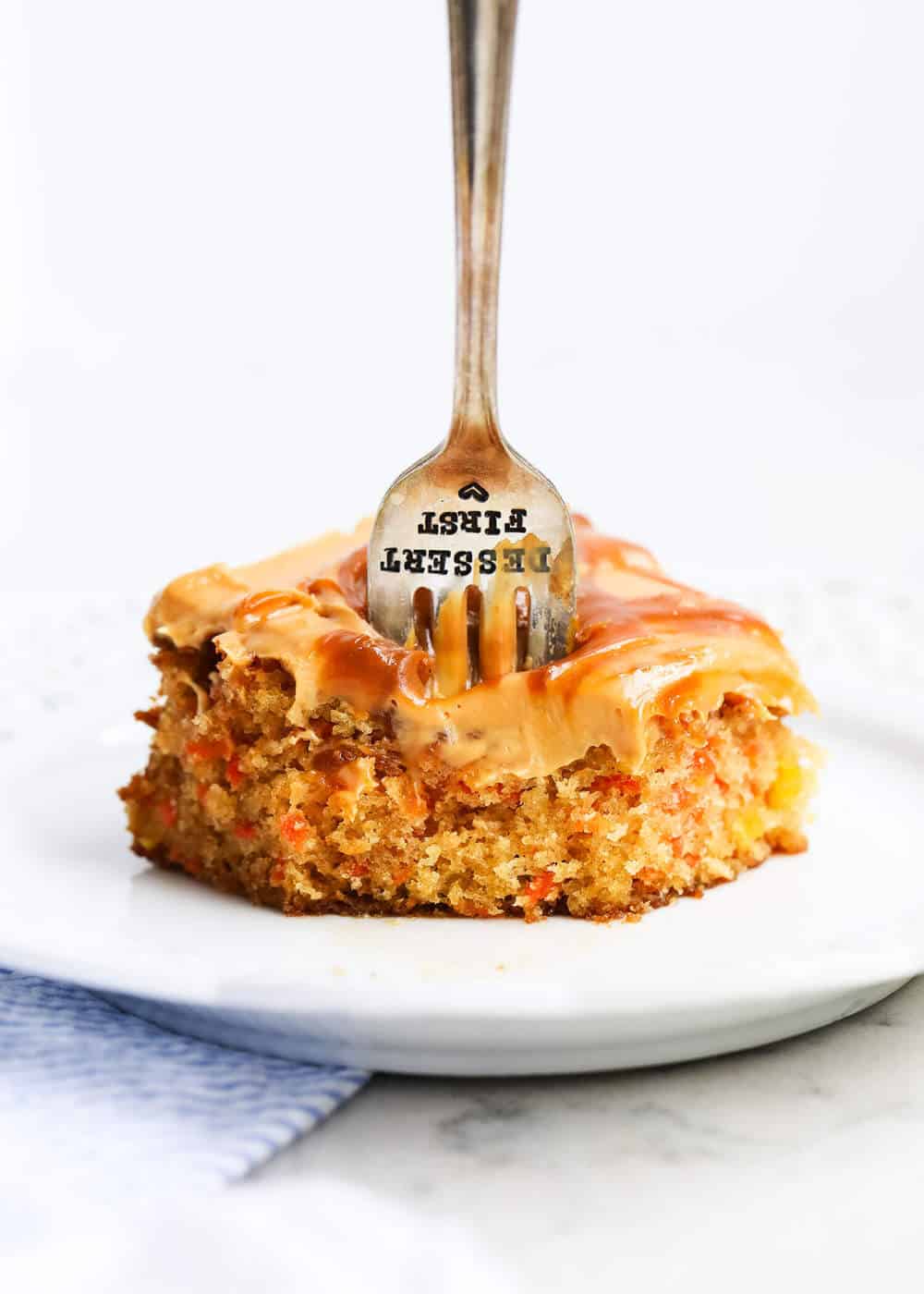 This caramel carrot cake is an easy fuss-free dessert that is a real crowd pleaser! Simple to make and deliciously moist, it’s topped with silky caramel cream cheese frosting. A slice of caramel carrot cake with a fork in it.
