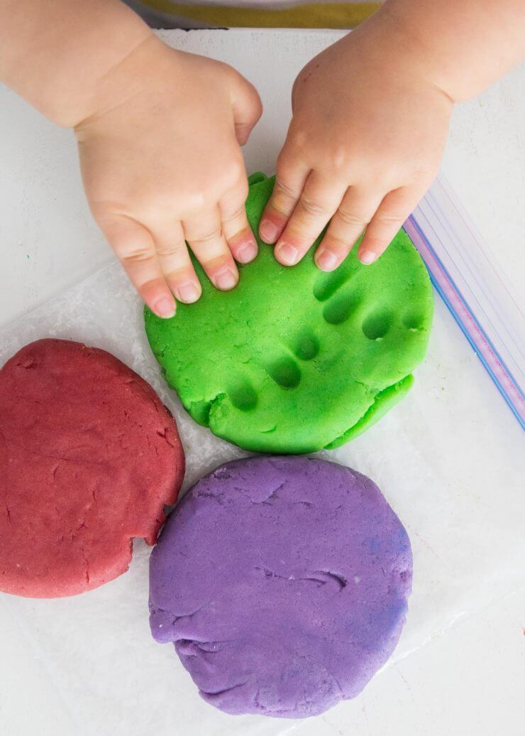 子供の手は遊びの生地の緑の部分を押し下げ's hands pressing down on a green piece of play dough