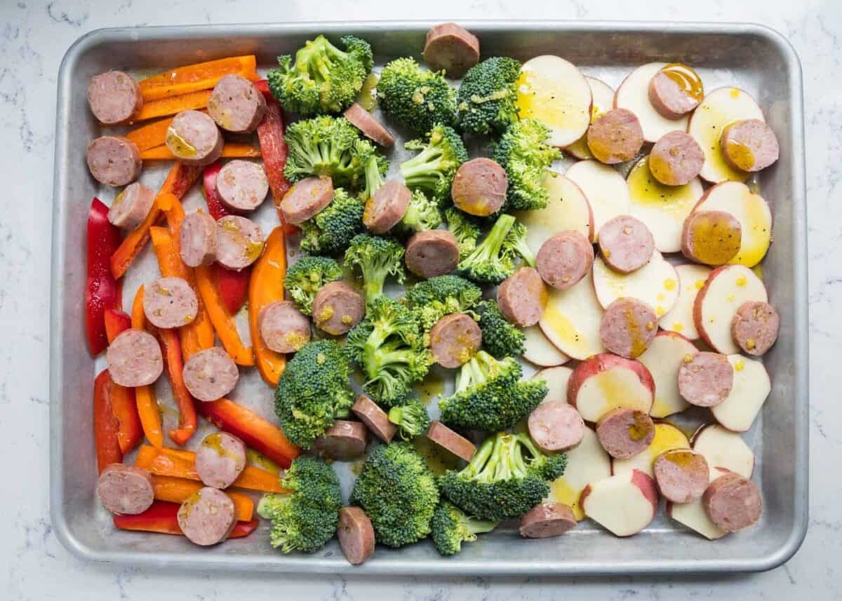 sausage and veggies drizzled with olive oil on baking sheet 