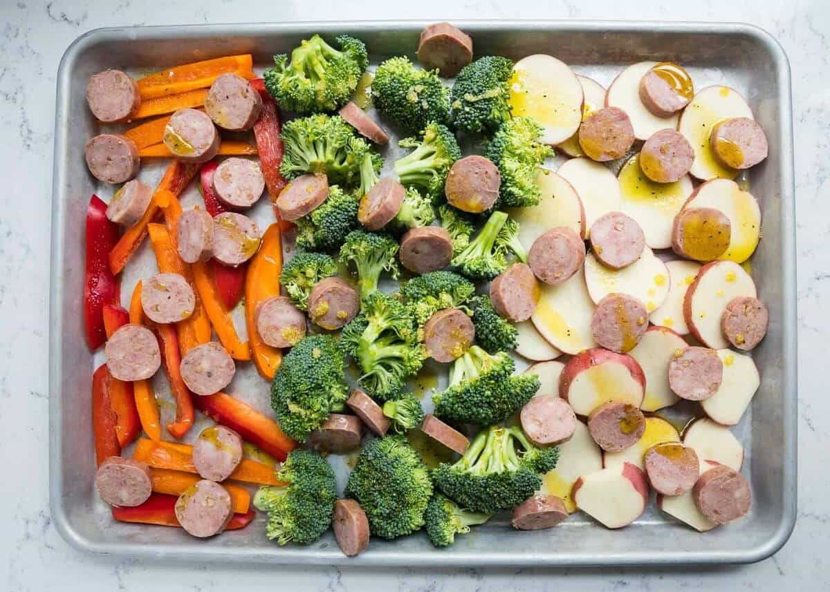 Sausage and veggies drizzled with olive oil on baking sheet.