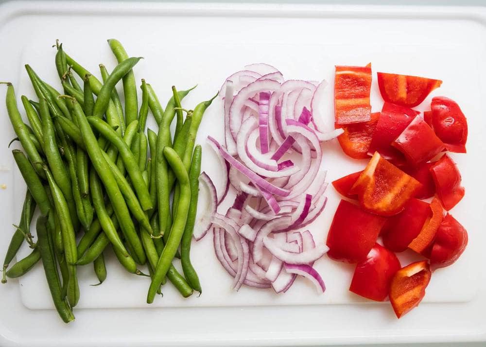 Green beans, sliced red onion and chopped red pepper on a cutting board.