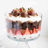layers of cream, strawberries, chocolate pudding and brownies in a glass trifle jar