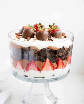 layers of cream, strawberries, chocolate pudding and brownies in a glass trifle jar