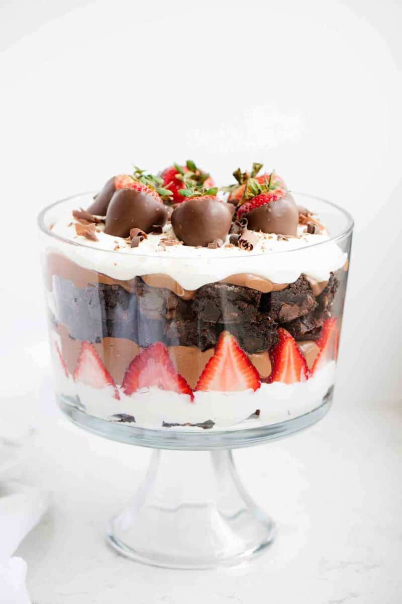 Layers of cream, strawberries, chocolate pudding and brownies in a glass trifle jar.