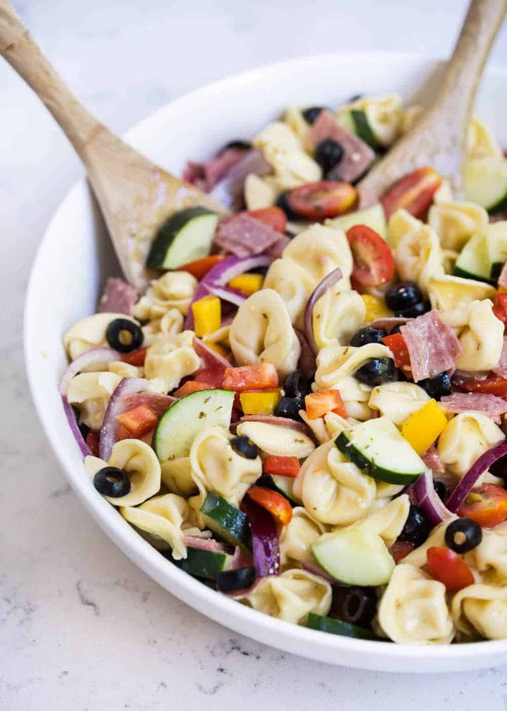 Italian tortellini pasta salad in a bowl with a wooden spoon.