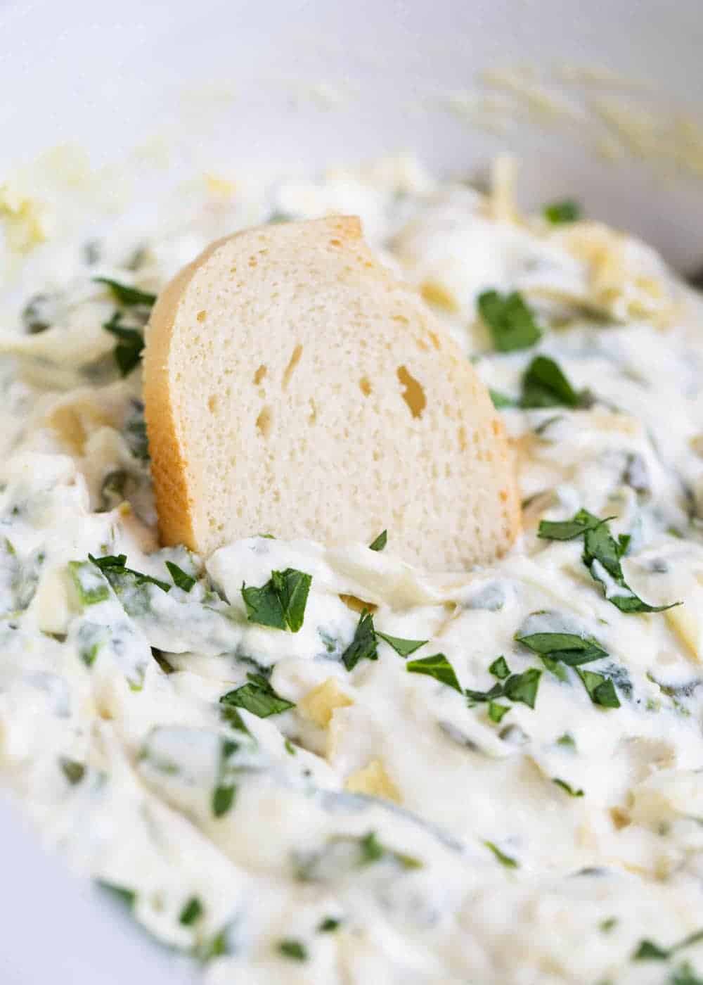 Baguette slice dipped in spinach artichoke dip.