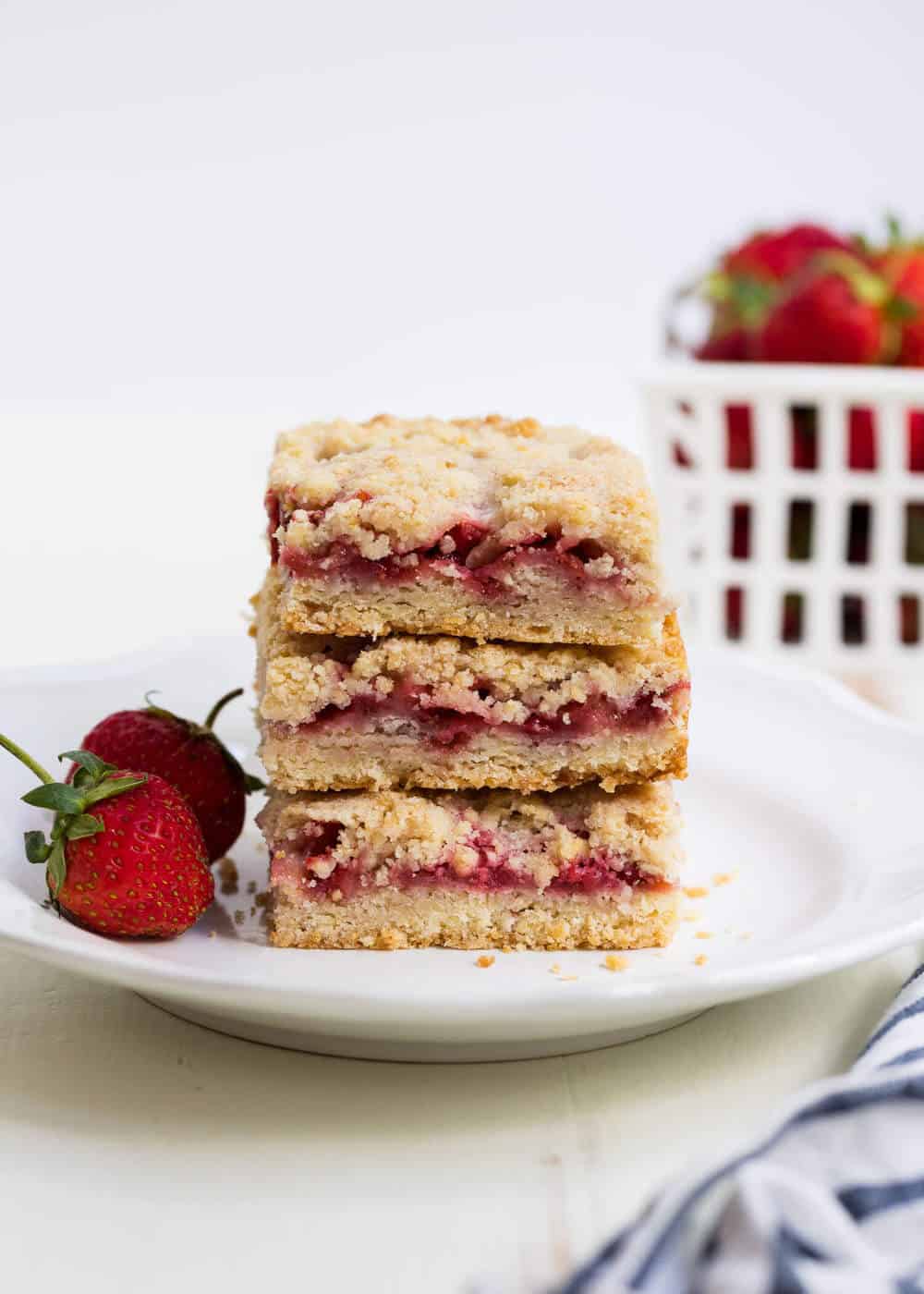 Strawberry crumb bars made with an easy crumb crust, strawberry filling and buttery crumb topping. The perfect summer dessert made with fresh, juicy strawberries! Stack of strawberry crumb bars on a white plate.