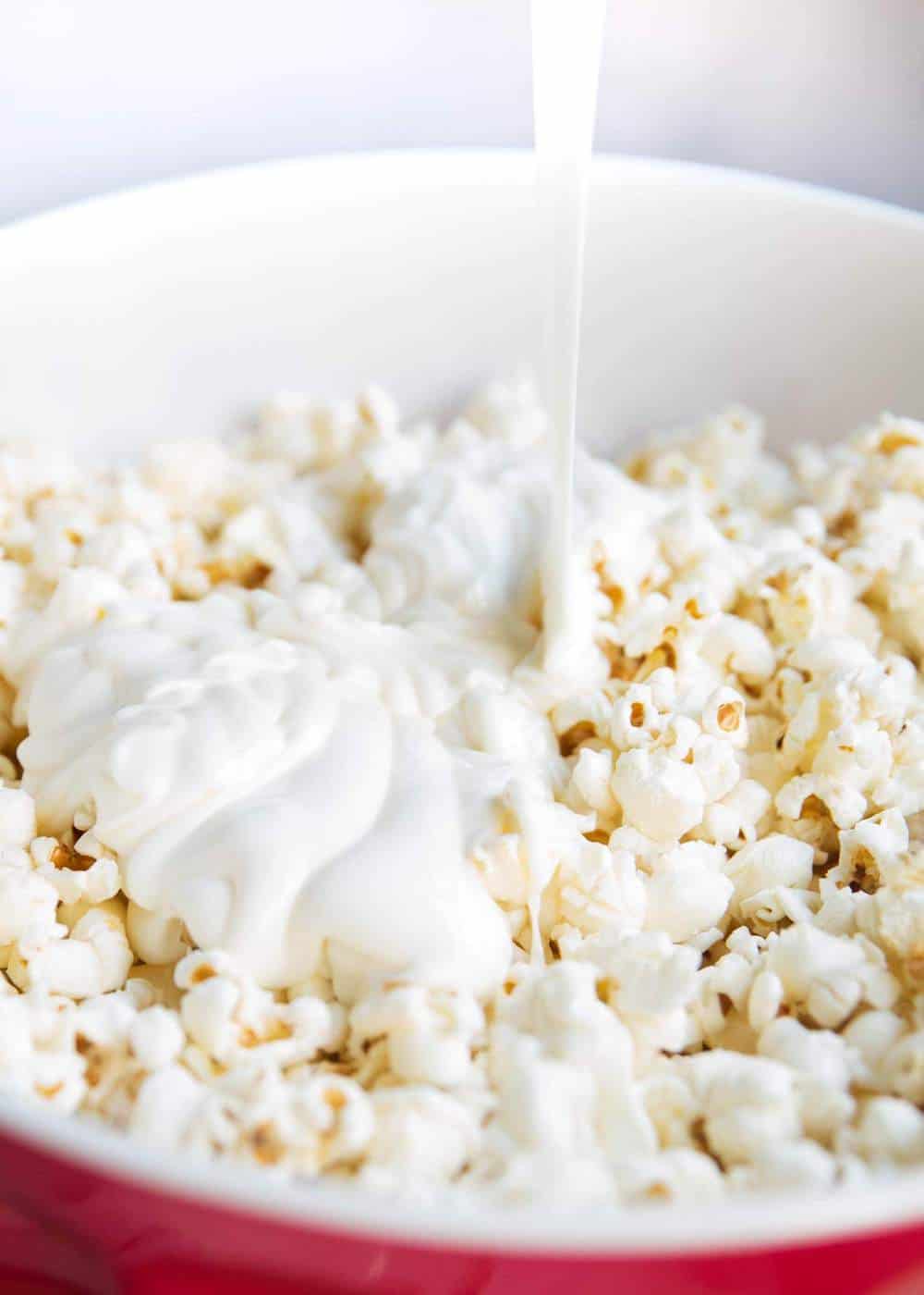 Pouring melted white chocolate over popcorn.