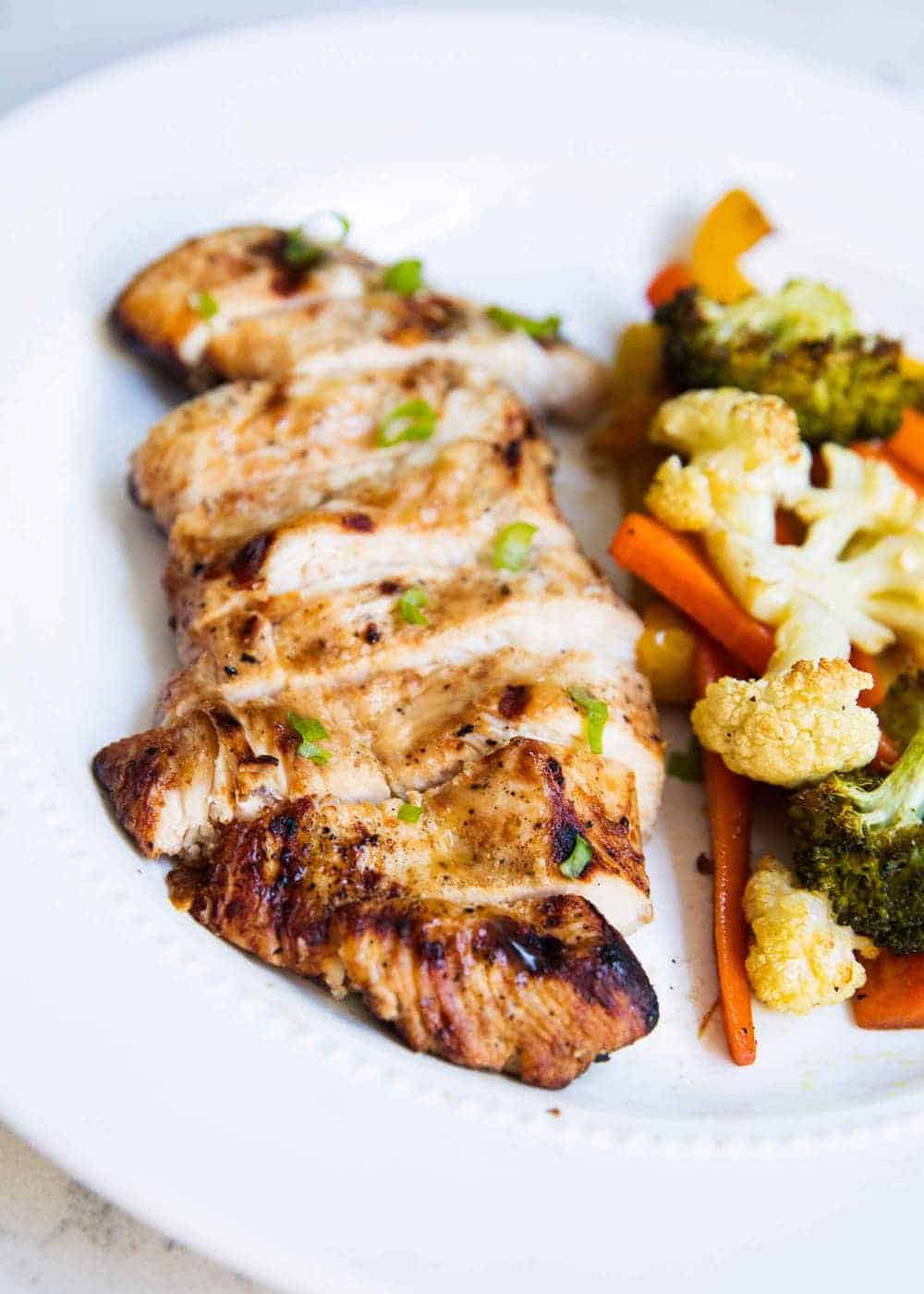 Sliced grilled chicken on plate with vegetables.