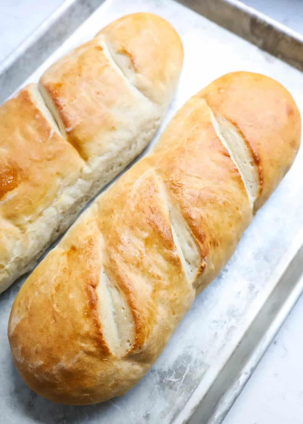 two homemade french bread loaves on a baking sheet 