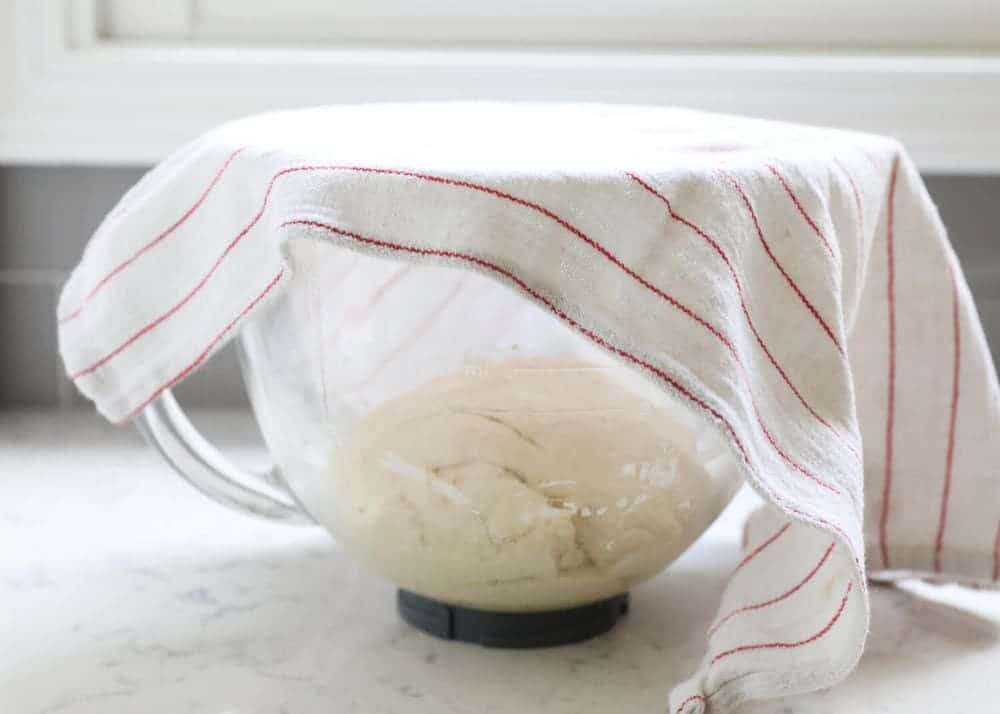 dough rising in a bowl with a dish towel on top 