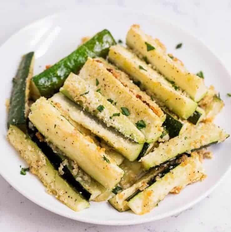 Parmesan baked zucchini fries stacked on a white plate.