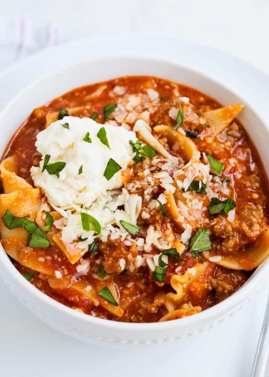 bowl of lasagna soup topped with ricotta and chopped basil 