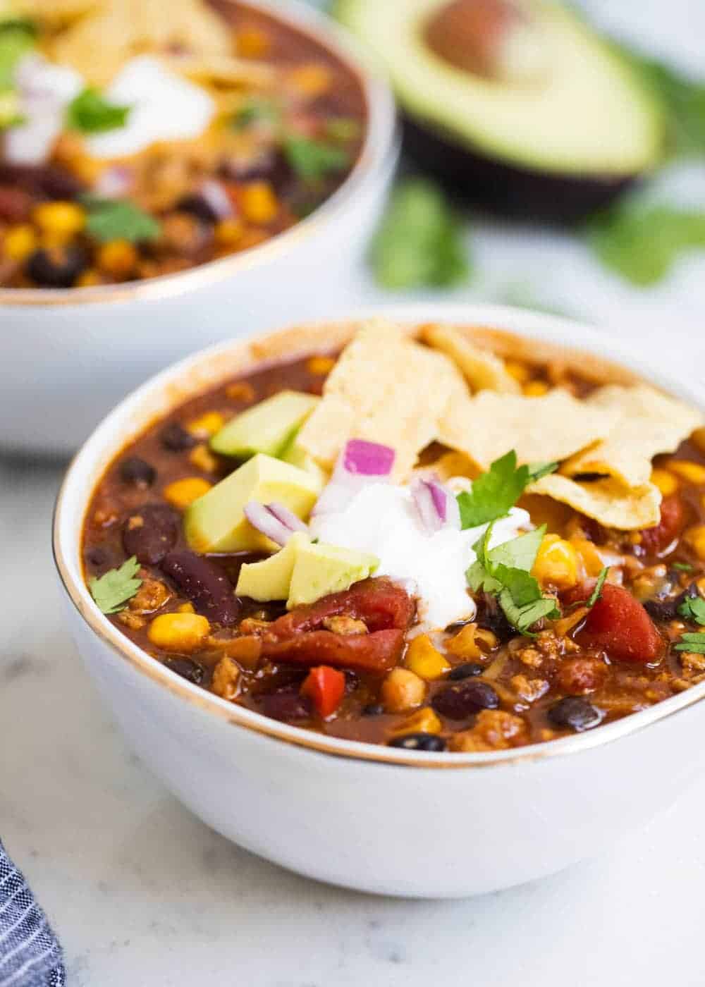 Bowl of healthy turkey chili with sour cream, red onion and crushed tortilla chips.
