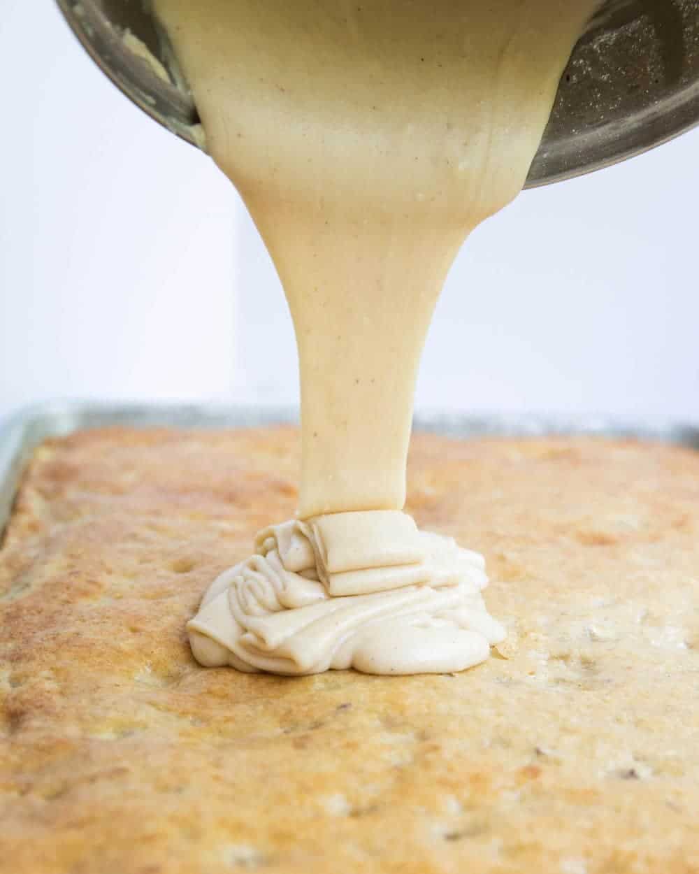 pouring brown butter frosting on top of banana bars 