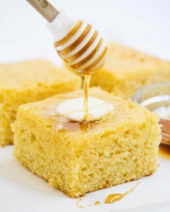 drizzling honey on top of a piece of sweet cornbread