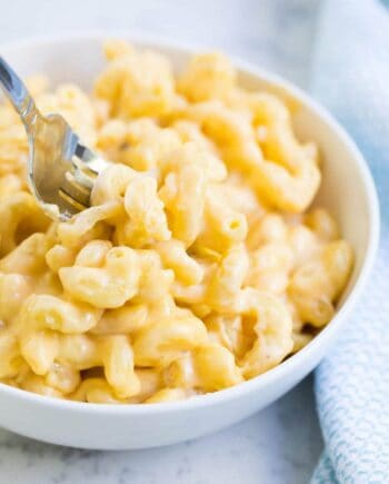 dipping a fork into a bowl of creamy macaroni and cheese
