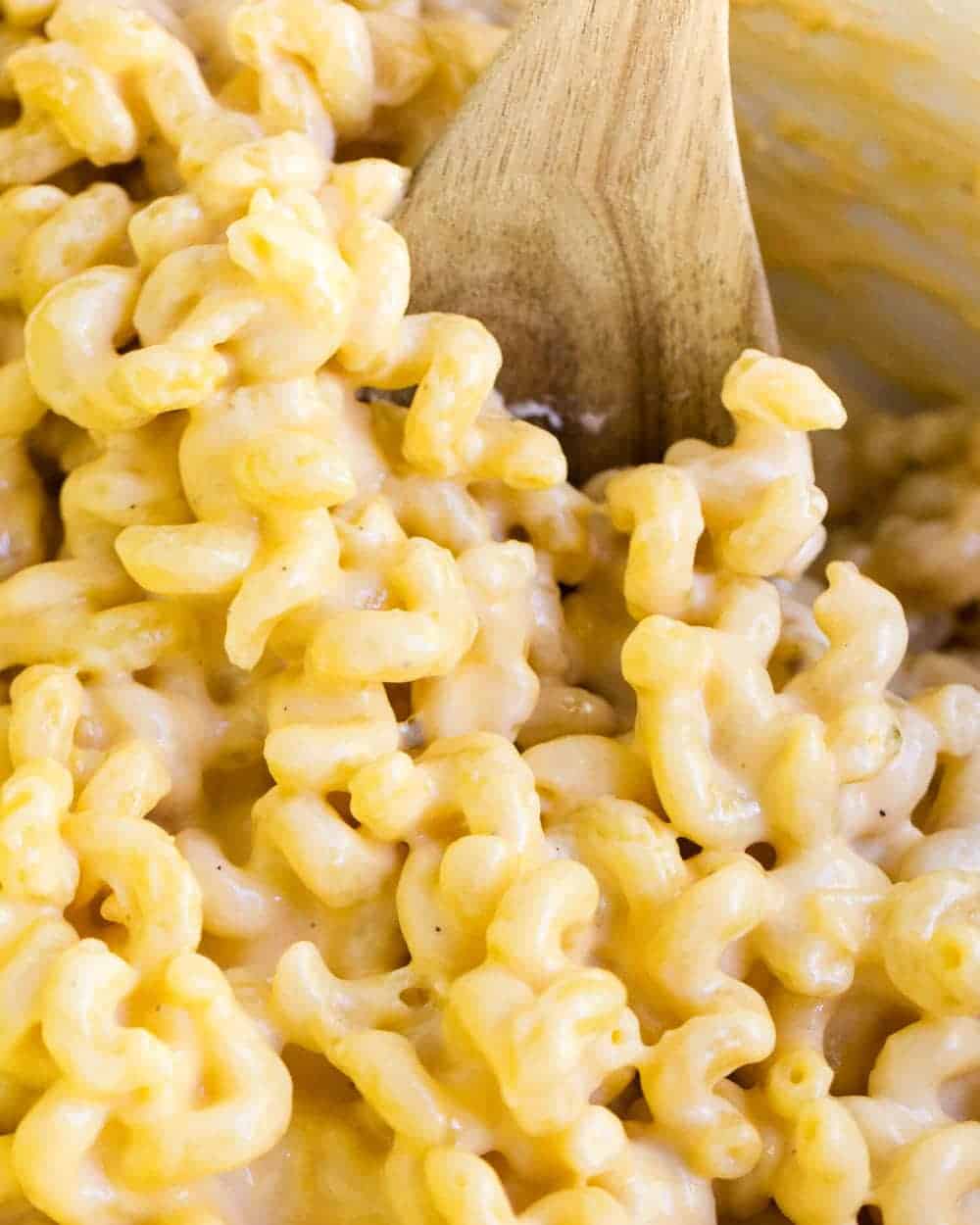 Slow cooker mac n cheese with a wooden spoon.