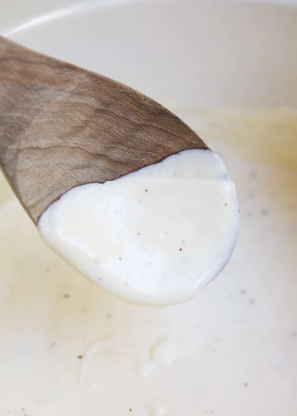 stirring cream cheese alfredo with a wooden spoon 