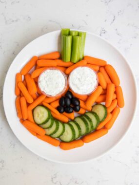 Halloween veggie tray in the shape of a pumpkin with mini carrots and creamy dip.