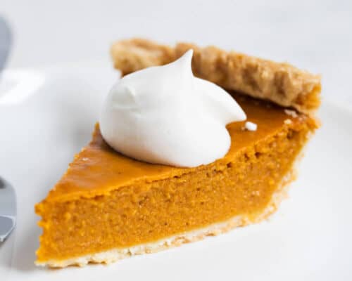 A piece of pumpkin pie on a plate with a dollop of whipped cream on top