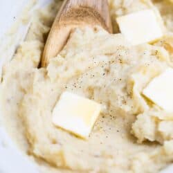 wooden spoon in slow cooker mashed potatoes with butter slices on top