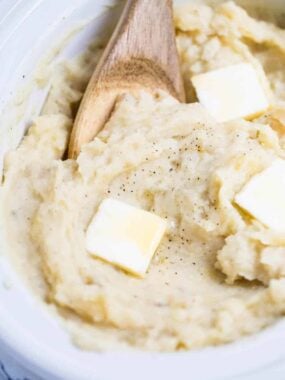 wooden spoon in slow cooker mashed potatoes with butter slices on top