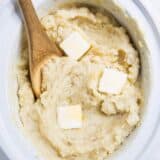 wooden spoon in slow cooker mashed potatoes with butter slices on top