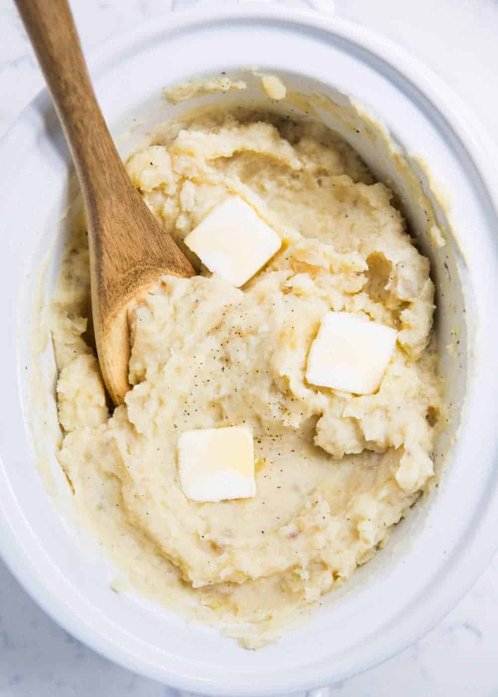 Mashed potatoes in the crock pot with a wooden spoon.