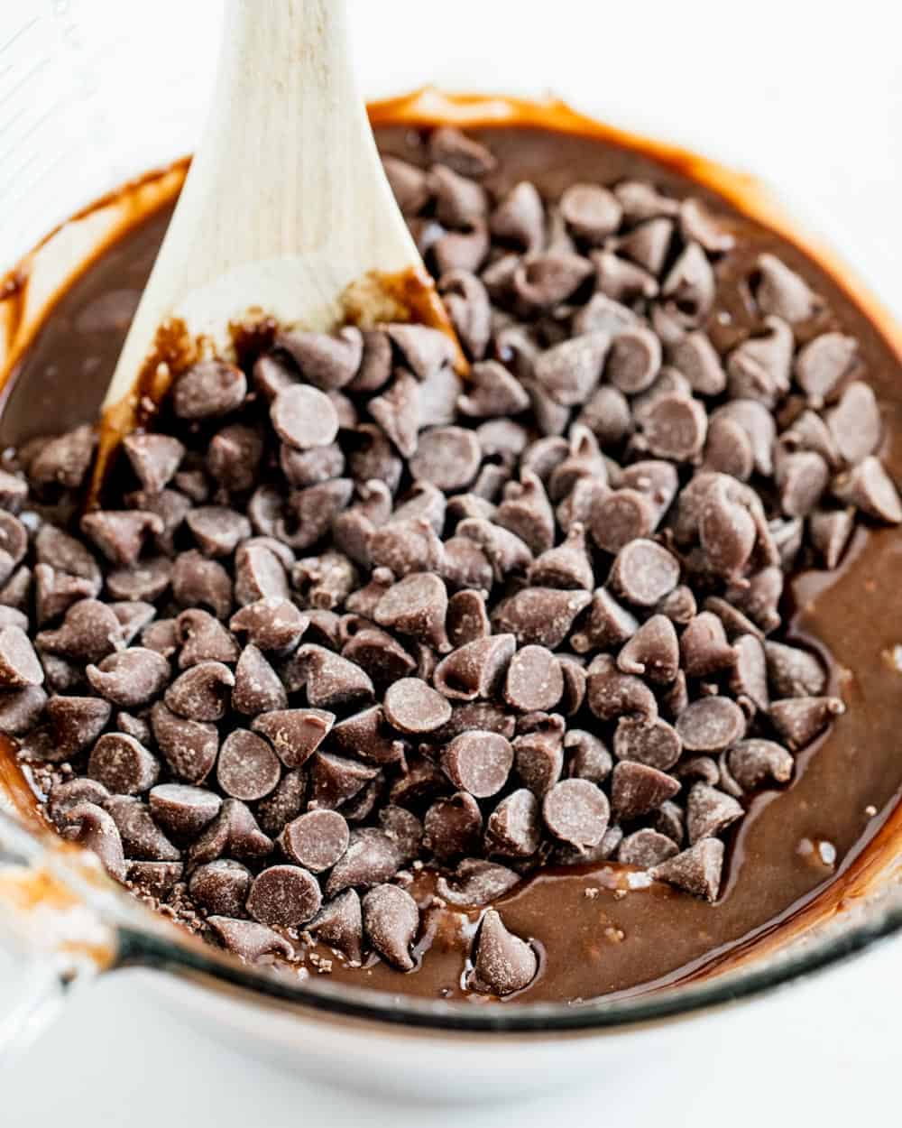 Folding chocolate chips into brownie batter with wooden spoon.