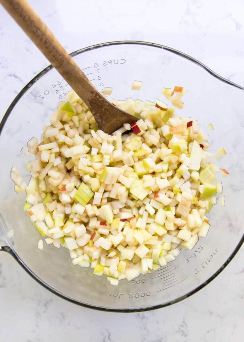 mixing together diced apples with spices in glass bowl 